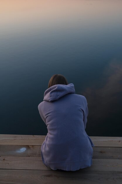 Foto frau, die auf dem pier sitzt, großporträt sommer sonnenuntergang