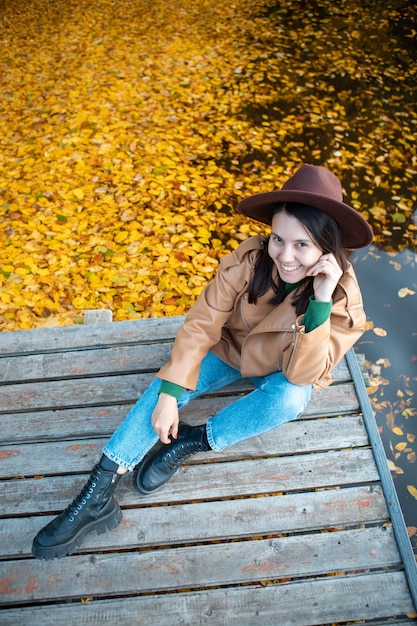 Frau, die auf dem Pier sitzt, sieht schöne Aussicht auf den Herbstsee mit Wald