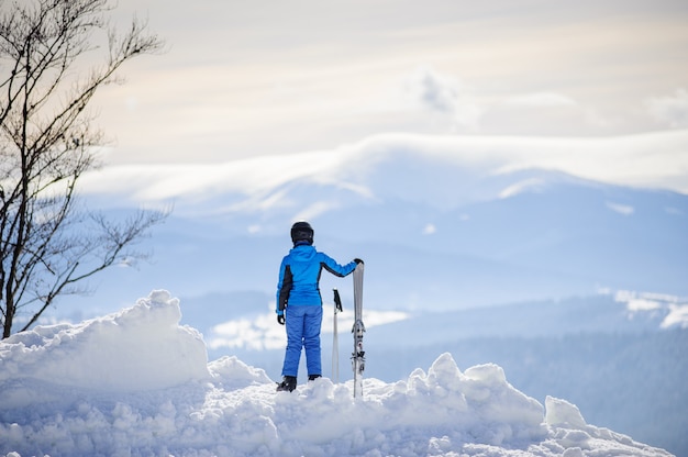 Frau, die auf den Berg steht und die Ansicht über schöne Winterberge genießt