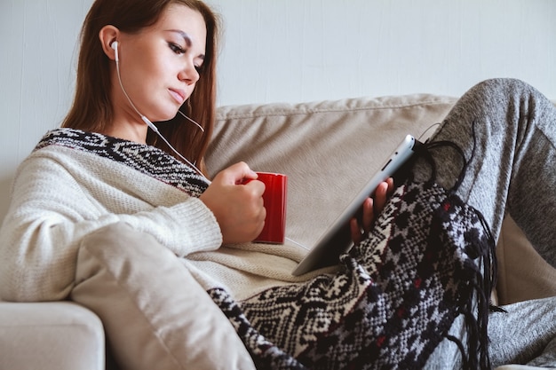 Frau, die auf der Couch mit Tablette und Kaffee in der Hand sitzt