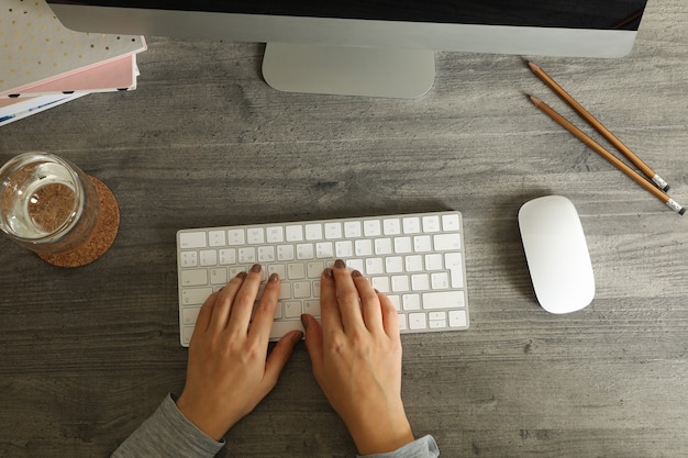 Frau, die auf Desktop-Computer auf grauem Holztisch arbeitet