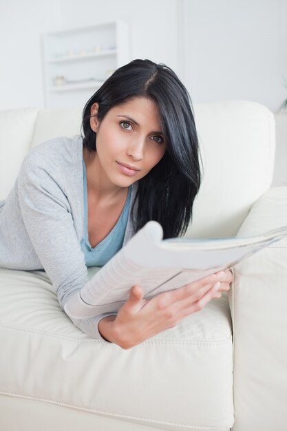 Frau, die auf eine Couch legt, während sie eine Zeitschrift hält