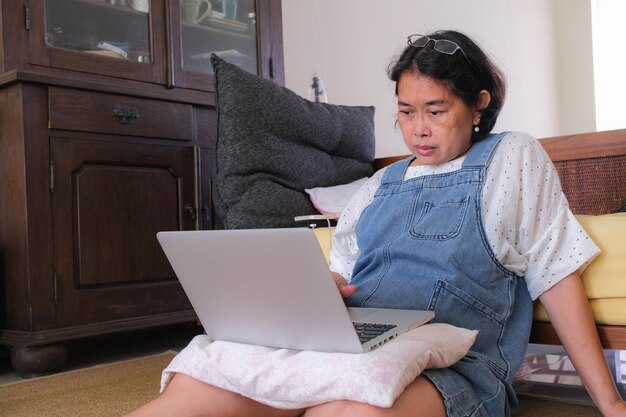 Frau, die auf einem Bodenteppich sitzt und zu Hause an ihrem Laptop arbeitet