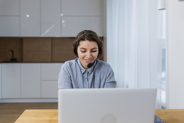 Frau, die auf einem Headset durch ein Laptopbuch im Büro spricht