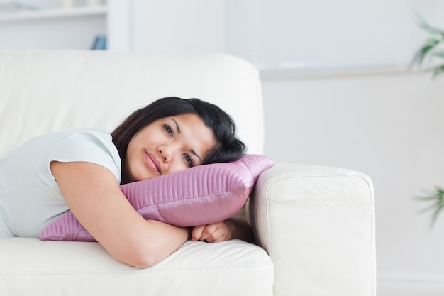 Frau, die auf einem Sofa beim Halten eines Kissens sich entspannt