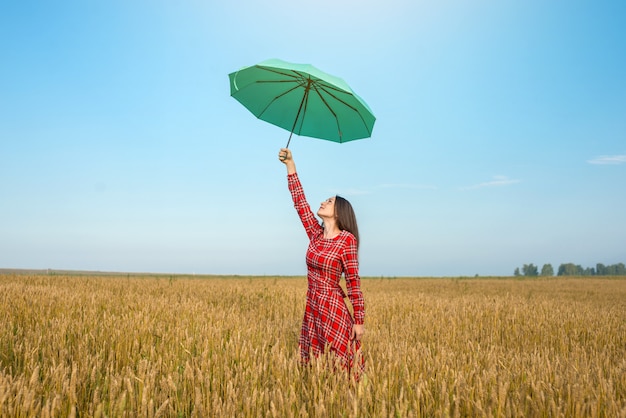 Frau, die auf einem Weizenfeld mit einem Regenschirm steht