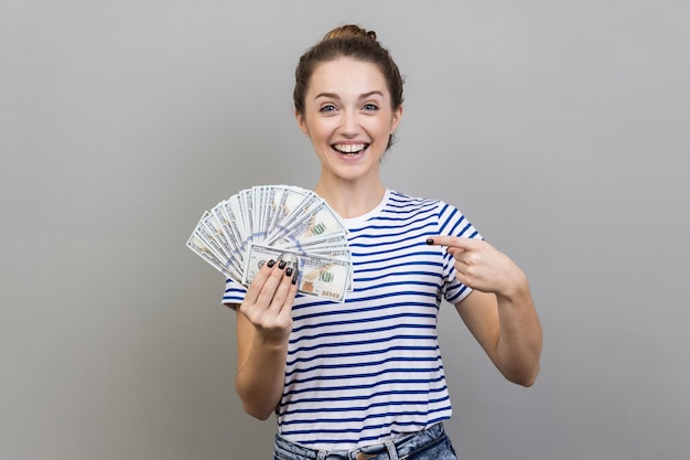 Frau, die auf einen Fan von Dollarbanknoten zeigt, die großes Geld zeigen und in die Kamera schauen