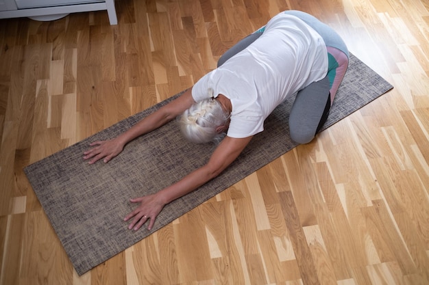 Frau, die auf einer Matte kniet und eine Balasana-Asana macht, während sie zu Hause Yoga praktiziert