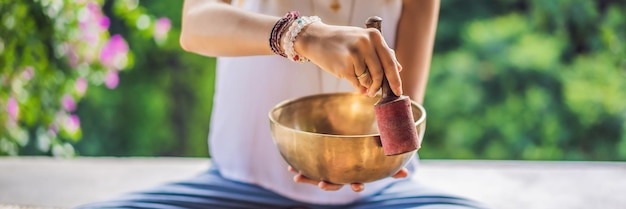 Frau, die auf einer tibetischen Klangschale spielt, während sie auf einer Yogamatte gegen einen Wasserfall-Vintage-Ton sitzt