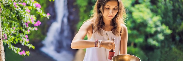 Frau, die auf einer tibetischen Klangschale spielt, während sie auf einer Yogamatte gegen einen Wasserfall-Vintage-Ton sitzt