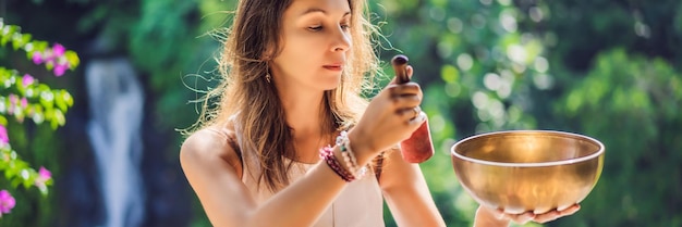 Frau, die auf einer tibetischen Klangschale spielt, während sie auf einer Yogamatte gegen einen Wasserfall-Vintage-Ton sitzt