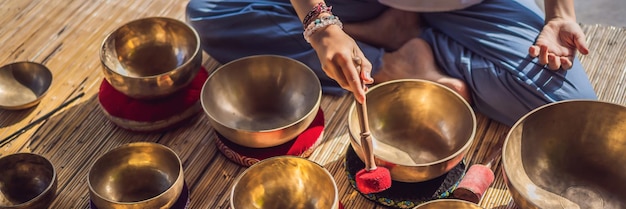 Frau, die auf einer tibetischen Klangschale spielt, während sie auf einer Yogamatte gegen einen Wasserfall-Vintage-Ton sitzt