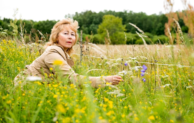 Frau, die auf Gras nahe dem Wald steht. Ältere Frau im Freien spazieren