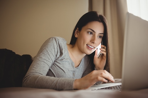 Frau, die auf Handy spricht, während Laptop verwendet wird