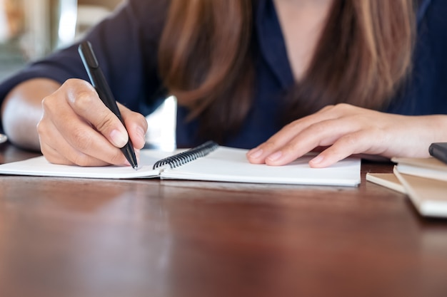 Frau, die auf leerem Notizbuch auf Tisch im Café schreibt