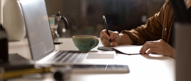 Frau, die auf leerem zeitplanbuch auf weißem tisch mit modell-laptop und zubehör im studio zur kenntnis nimmt