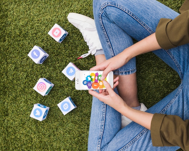 Frau, die auf Rasen unter Verwendung der Social Media-APP auf Mobiltelefon sitzt