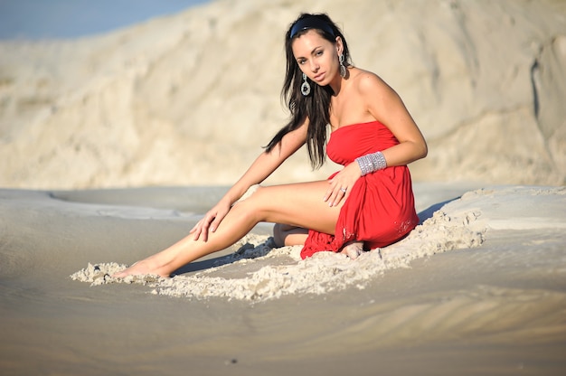 Foto frau, die auf sand im roten kleid kühlt