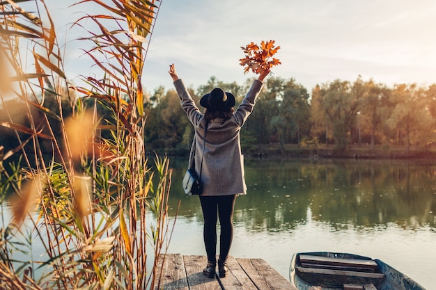 Frau, die auf Seepier durch das Boot anhebt Hände und bewundert Herbstlandschaft geht. Herbstsaison Aktivitäten