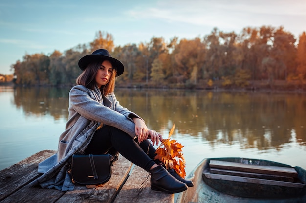 Frau, die auf Seepier durch das Boot bewundert Herbstlandschaft sitzt. Herbstsaison Aktivitäten