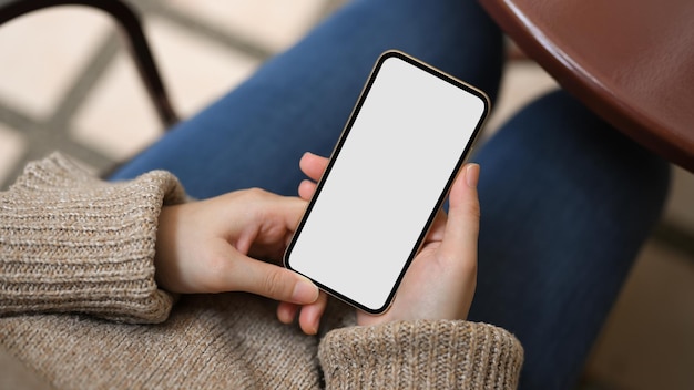 Frau, die auf Stuhl sitzt und mobile Anwendung auf dem leeren Bildschirm des Smartphones verwendet