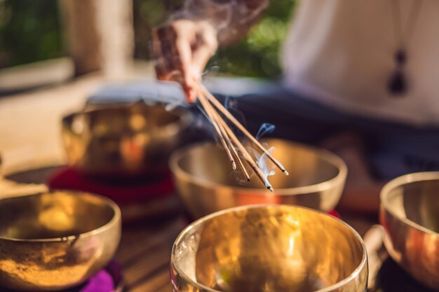 Frau, die auf tibetischer Klangschale spielt, während sie auf Yogamatte gegen einen Wasserfall sitzt Vintage getönt Schönes Mädchen mit meditierenden Mala-Perlen