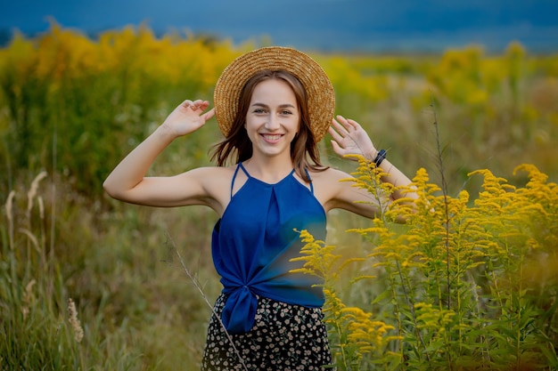 Frau, die auf Wildblumen-Feld bleibt, das weg Copyspace schaut. Lächelnd attraktive junge Mädchen Brünette trägt stilvolle Kleidung und Hut Aufenthalt auf landwirtschaftlichen Blumen Valley.