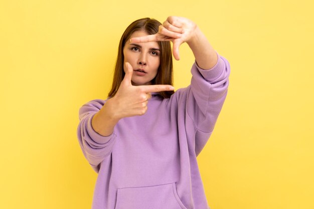 Frau, die aufmerksam durch die Form des Fotorahmens schaut, mit den Fingern, die eine fotografische Geste machen