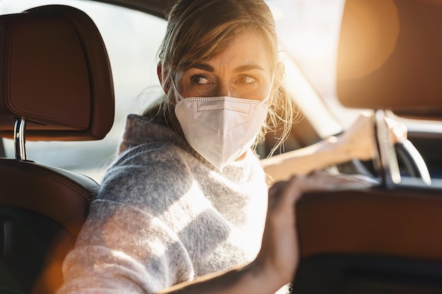 Frau, die Auto mit einer N95-FFP2-Antivirenmaske fährt, Schutzmaske gegen Coronavirus-Fahrer auf einer Stadtstraße, die während eines Coronavirus-Ausbruchs covid19 zurückschaut, während sie rückwärts fährt