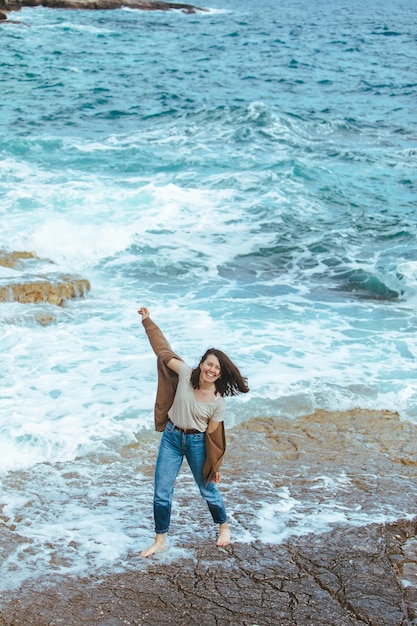 Frau, die barfuß in nassen Jeans am felsigen Strand spazieren geht