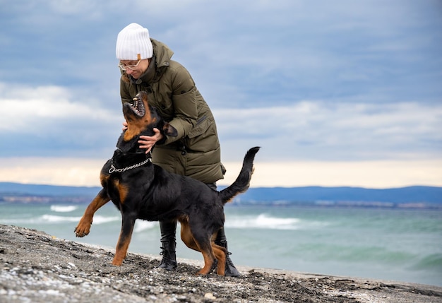 Frau, die bei kaltem Wetter am Strand mit Rottweiler-Hund herumalbert