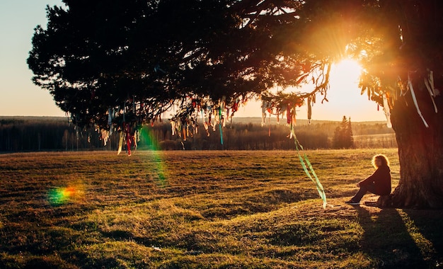 Frau, die bei Sonnenuntergang unter einem einsamen Baum sitzt