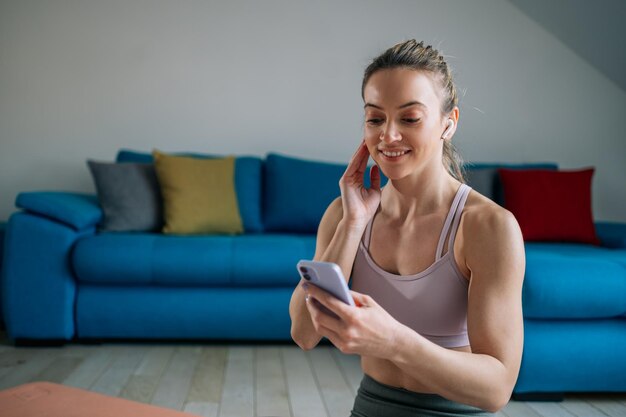 Frau, die beim Training zu Hause Airpods und ein Smartphone verwendet