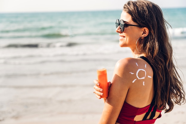 Frau, die Bikini trägt, der Sonnencreme mit Sonne an zurück am Strand anwendet