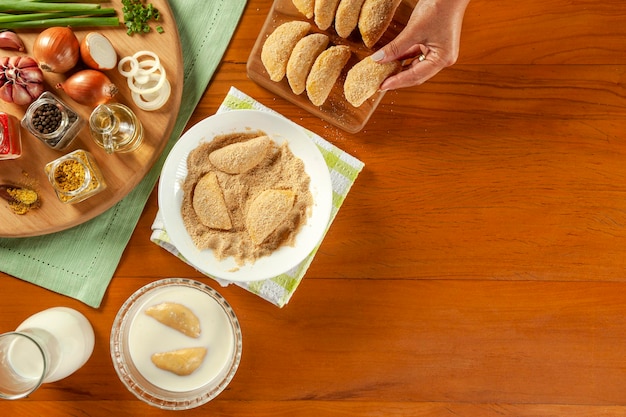 Frau, die brasilianisches Fleisch paniert, gefüllte Krokette Risolis de Carne auf einem Holztisch Draufsicht