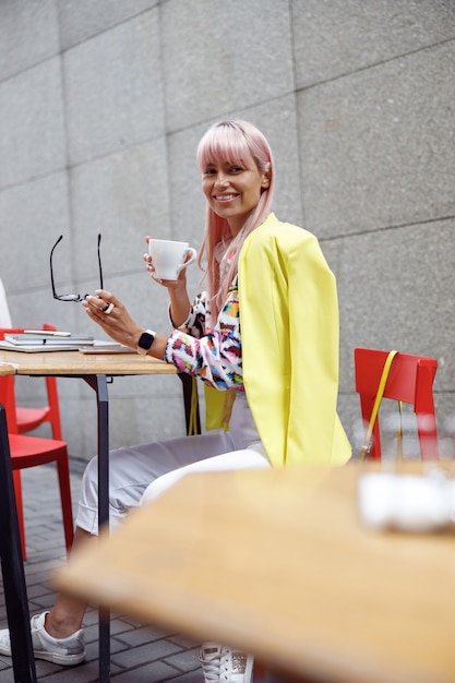 Frau, die Brille abnimmt und mit Kaffee in die Kamera lächelt