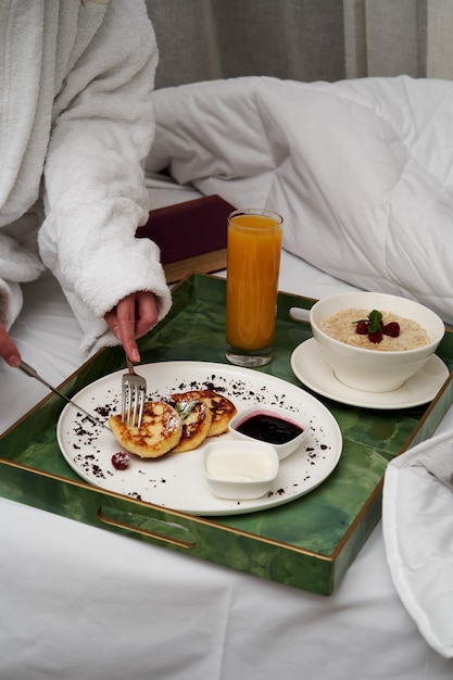 Frau, die Buch beim Frühstück im Bett liest. Frau im Bademantel beim Frühstück im Hotelbett, Nahaufnahme