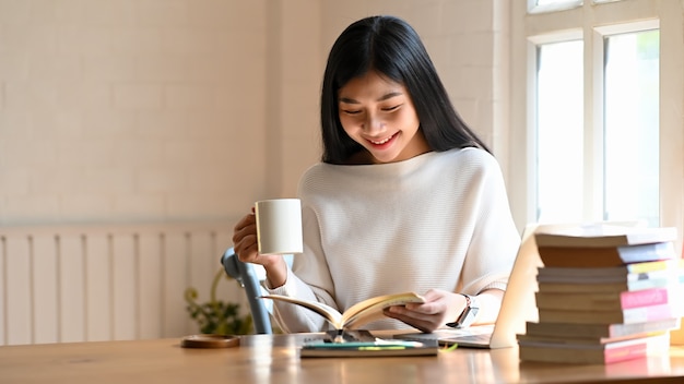 Frau, die Buch liest und ihren Kaffee im Hauptbüro hält.