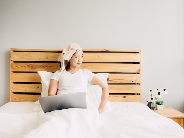 Frau, die Computer auf ihrem Bett am gemütlichen Sonntagmorgen verwendet