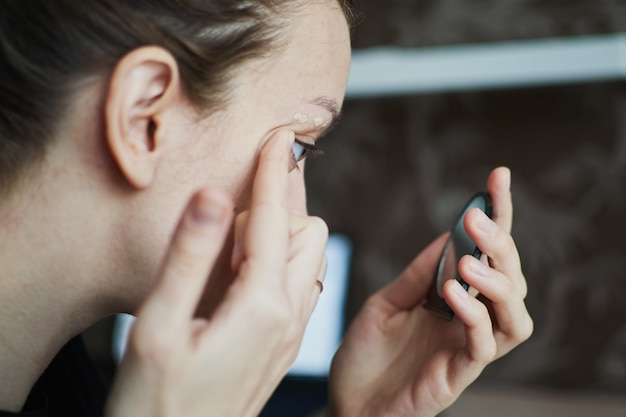 Frau, die Creme und Blicke auf einen Handspiegel aufträgt