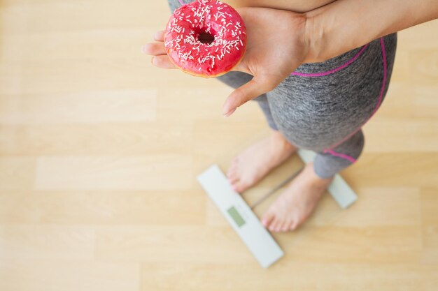 Foto frau, die das körpergewicht auf einer waage mit donut misst