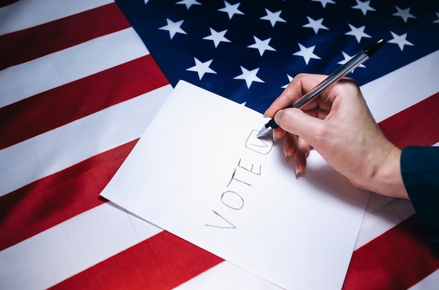 Foto frau, die das papier zur abstimmung ankreuzt. politische veränderungen im land. platz kopieren. wahlen in den usa. amerikanische flagge. leute, die auf stimmzettel abstimmen.