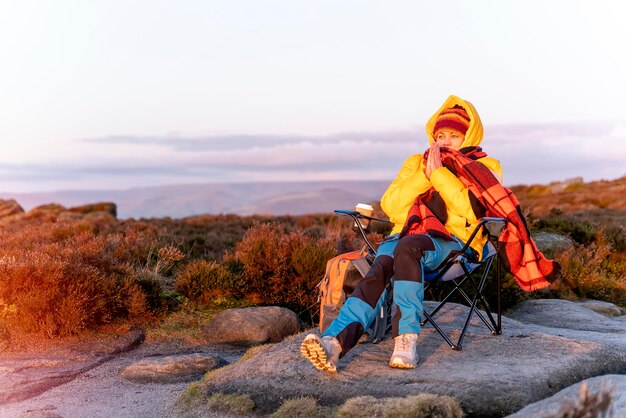 Frau, die das Ziel erreicht und bei Sonnenaufgang auf Liegestühlen auf einem Hügel oder Berg sitzt