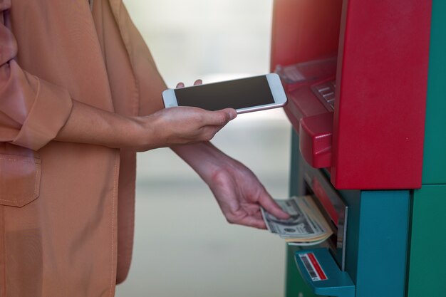 Frau, die den intelligenten Handy für das Zurückziehen vor dem ATM verwendet