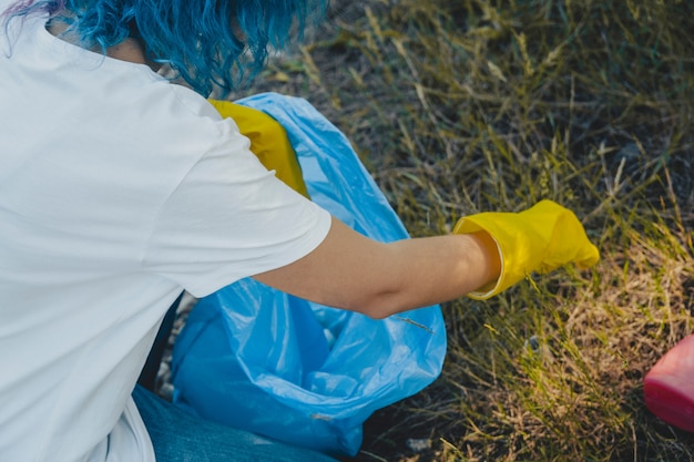 Frau, die den Plastikmüllsack in einer grünen Umgebung leert - Plastikverschmutzungskonzept