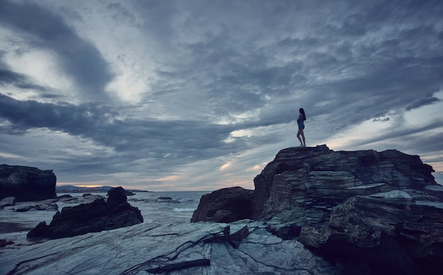 Frau, die den Sonnenuntergang am Strand beobachtet. Catedrales Strand an der Küste von Galizien