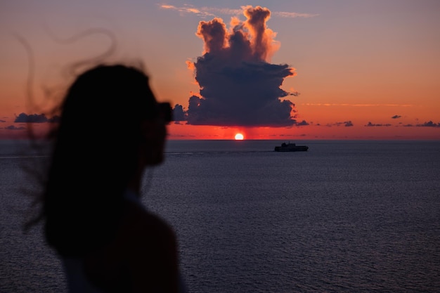 Frau, die den sonnenuntergang über dem seeschiff im hintergrund betrachtet