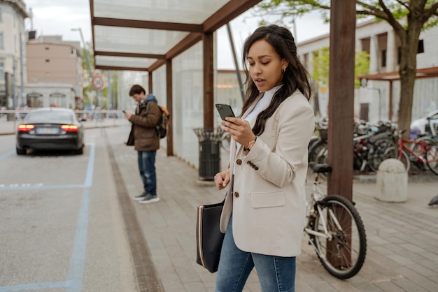 Frau, die die Handykommunikation online nutzt und eine Textnachricht liest, die am Busbahnhof steht