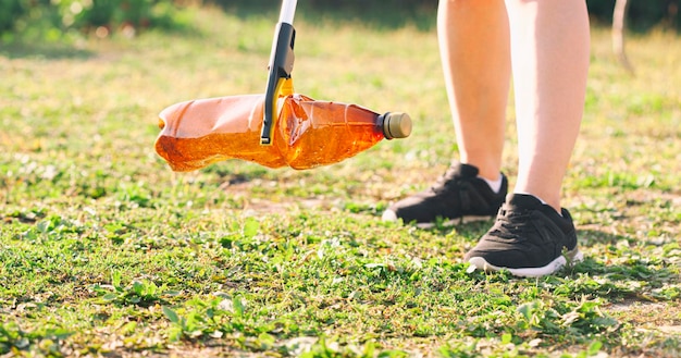 Frau, die die Plastikflasche mit dem Müllsammelwerkzeug auswählt