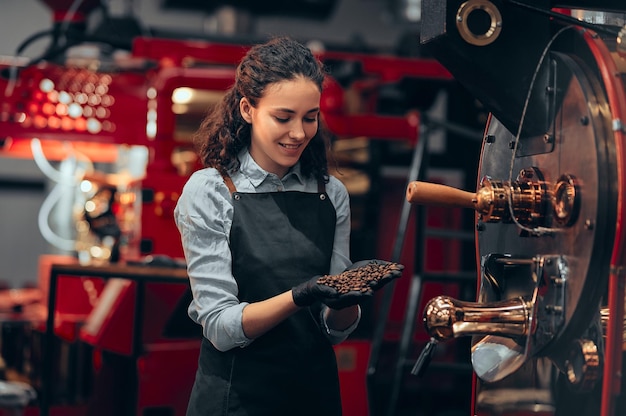 Frau, die die Qualität der Kaffeebohnen überprüft, die in der Nähe der Röstermaschine in der Rösterei stehen